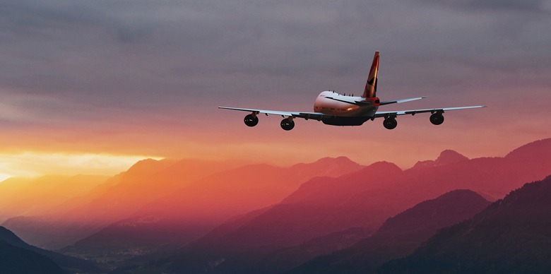 A commercial airplane soars above majestic mountains during a vibrant sunset, highlighting the contrast between technology and nature.
