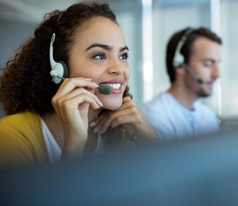 Support agent smiling while on a call in a modern office. Focus on providing excellent customer service in a collaborative environment.